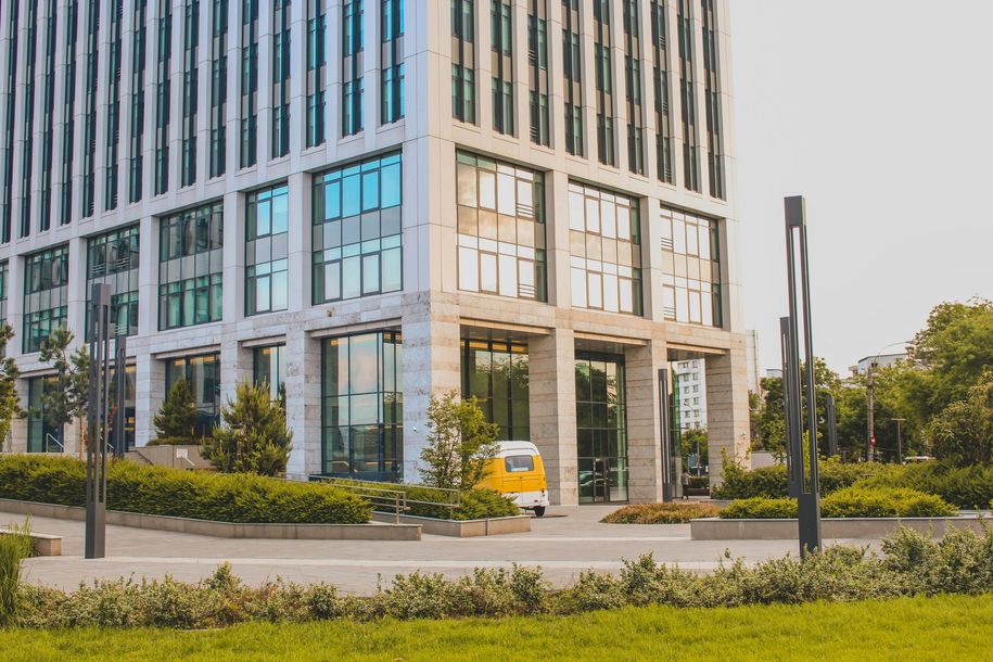 Modern office building with glass windows, a yellow delivery van, and green landscaping in front